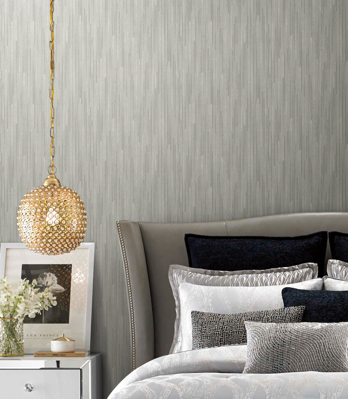 A bedroom featuring grey Candice Olson Bargello Wallpaper with vertical-striped texture, a crystal pendant light, and a bed with layered pillows.