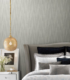 A bedroom featuring grey Candice Olson Bargello Wallpaper with vertical-striped texture, a crystal pendant light, and a bed with layered pillows.