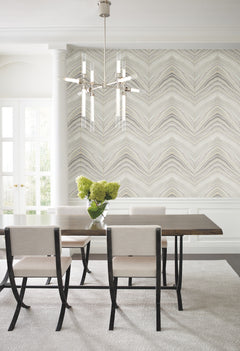 A dining room featuring Candice Olson Onyx Strata Wallpaper with a beige and grey chevron pattern, a dark wood table with upholstered chairs, and a glass vase with greenery.