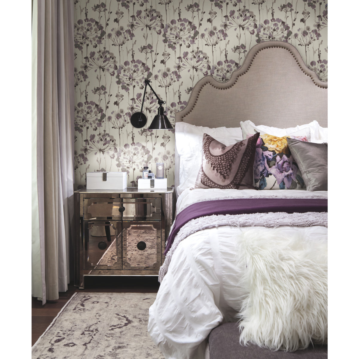 A bedroom features Candice Olson Flourish Wallpaper with a purple and grey botanical print behind an upholstered headboard and a mirrored nightstand.