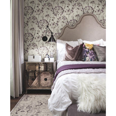 A bedroom features Candice Olson Flourish Wallpaper with a purple and grey botanical print behind an upholstered headboard and a mirrored nightstand.