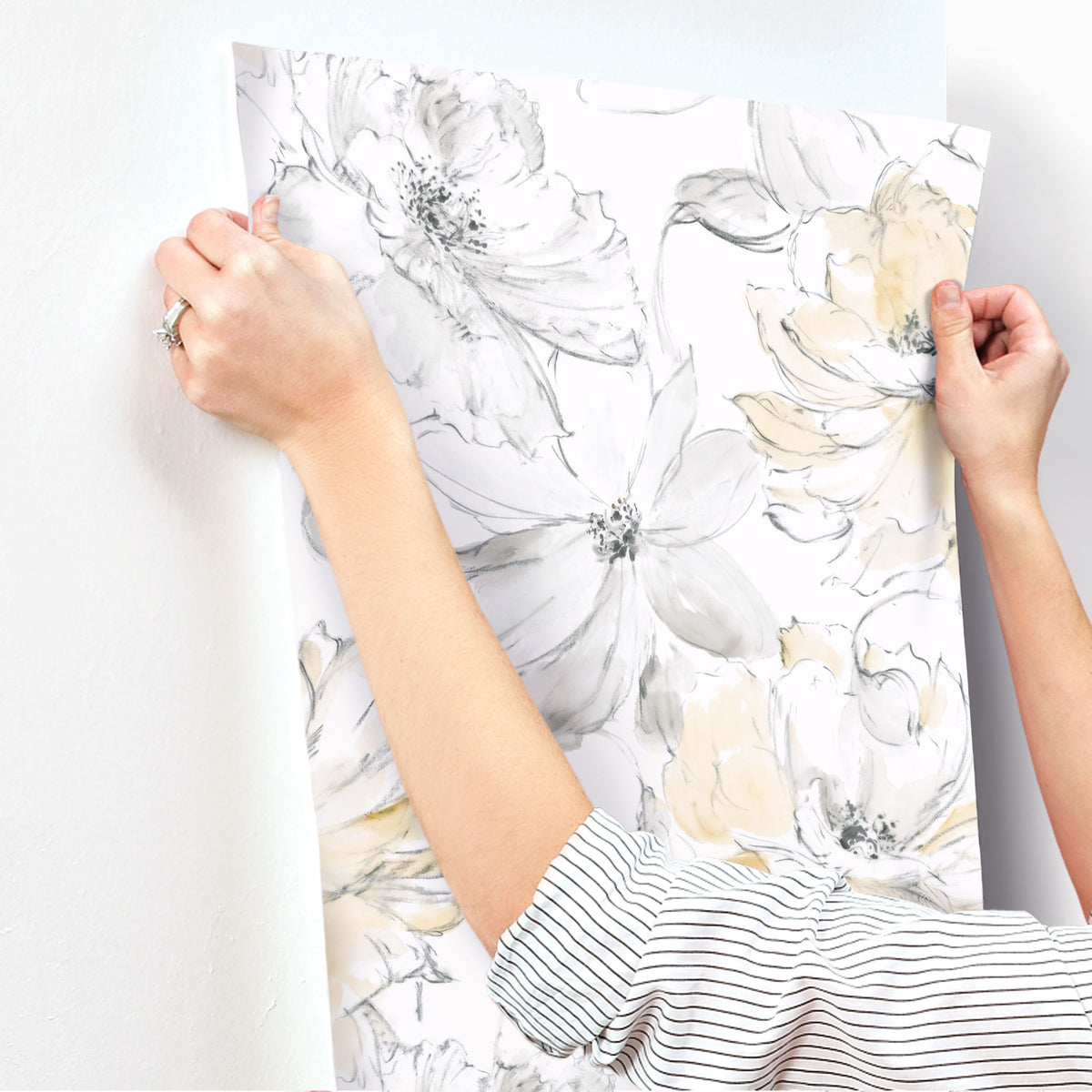 Hands applying Floral Dreams Wallpaper featuring watercolor-style gray and yellow flowers to a white wall.