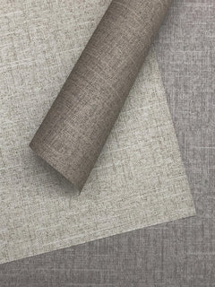 A roll of textured, taupe-colored Candice Olson Errandi Wallpaper by York Wallcoverings placed diagonally across a matching sheet of the same material.