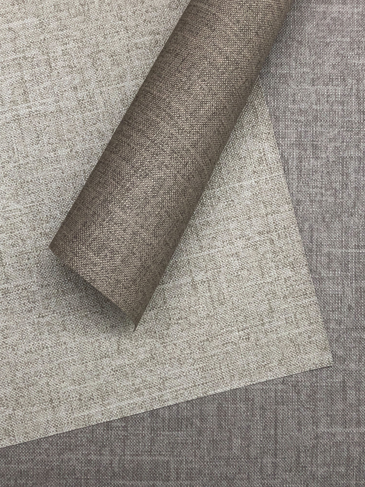 Stacked rolls of Candice Olson Errandi Wallpaper by York Wallcoverings featuring a neutral, fabric-like textured pattern in shades of beige and gray.