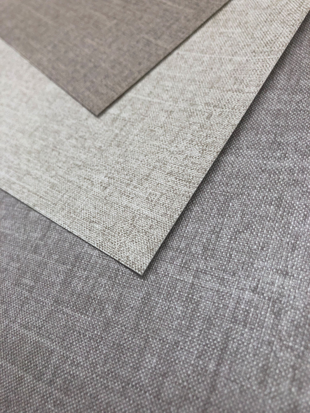 Three overlapping samples of Candice Olson Errandi Wallpaper by York Wallcoverings in shades of taupe, beige, and grey with a subtle woven texture.