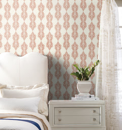 An elegant bedroom featuring a cream upholstered headboard, a nightstand with a potted plant, and cream Broadsands Botanica Wallpaper by York Wallcoverings adorned with a pink leaf pattern. A sheer white curtain with script text partially covers the window.