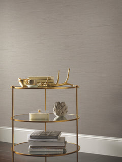 A gold three-tiered shelf holds decorative items—including a gold bowl, antler, artichoke sculpture, small box, and neatly stacked books—set against a backdrop of York Wallcoverings Ribbon Bamboo Wallpaper.