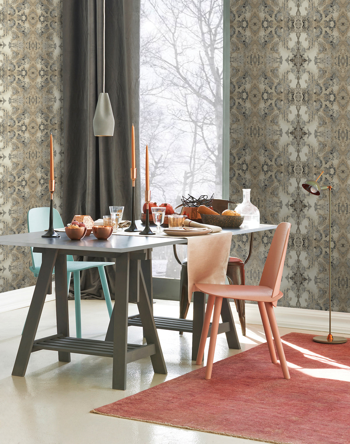 A dining table set for a meal against Inner Beauty Wallpaper by York Wallcoverings, featuring two chairs in different colors, tall candlesticks, and a view of trees through a window.