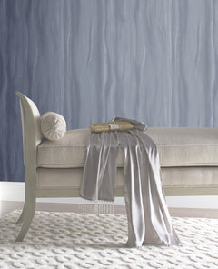 A beige upholstered bench with a round bolster cushion, a gold clutch, and a draped silver scarf, set against Candice Olson Fantasy Faux Bois Wallpaper by York Wallcoverings.
