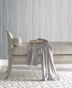 An upholstered bench with a small bolster pillow, a gold clutch, and a draped gray scarf, set against York Wallcoverings Candice Olson Fantasy Faux Bois Wallpaper featuring a white wood-grain pattern.