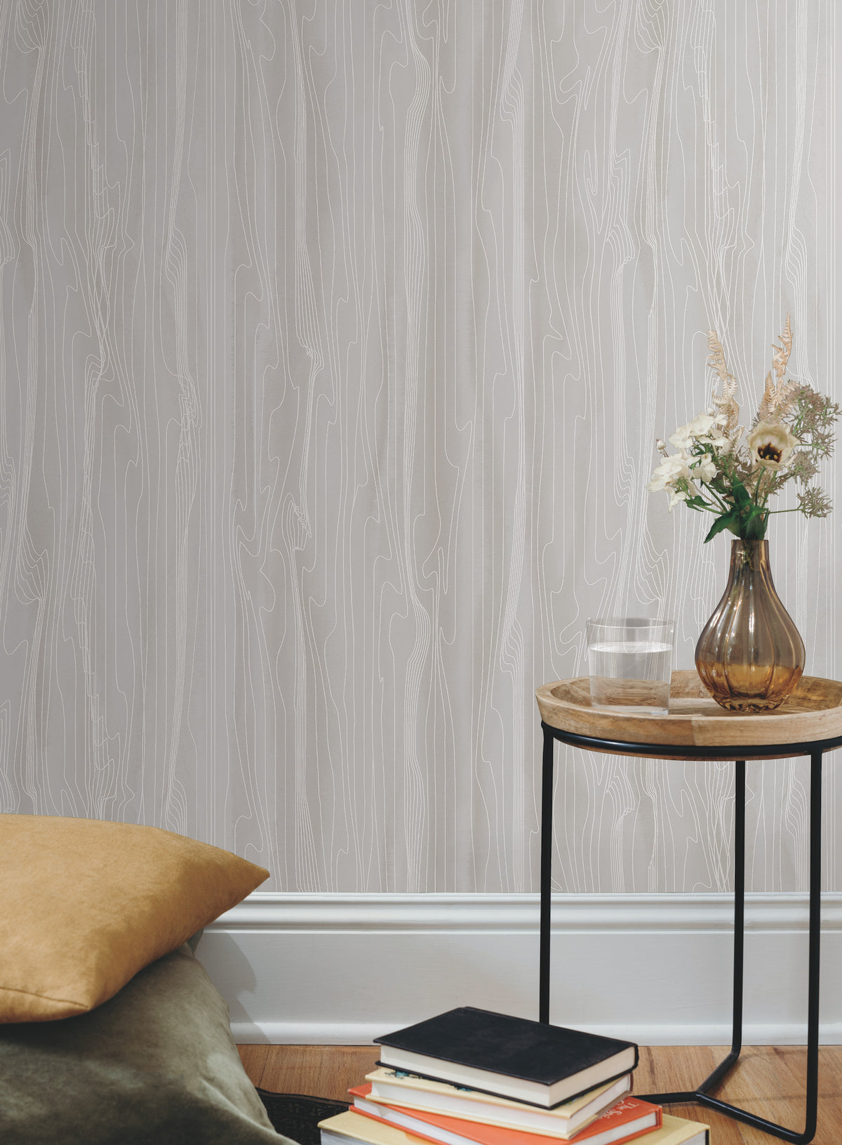 Candice Olson Fantasy Faux Bois Wallpaper in light gray with a linear wood grain pattern displayed behind a side table with a glass of water and a floral arrangement.