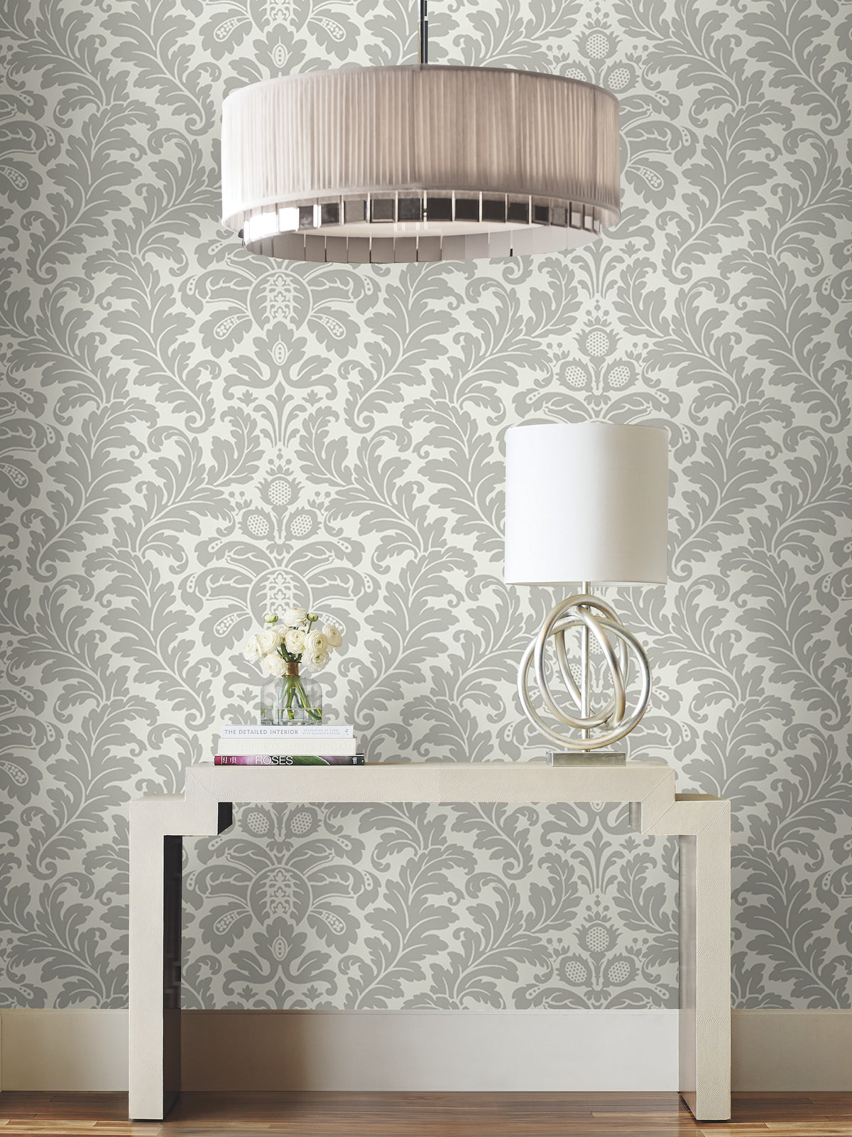 Candice Olson Modern Romance Wallpaper in a grey and white damask pattern on a wall behind a console table with a lamp and vase of flowers.
