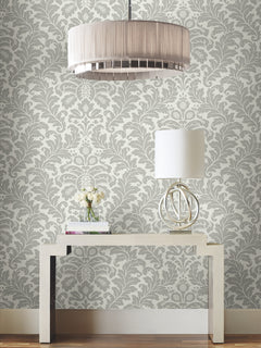 Candice Olson Modern Romance Wallpaper in a grey and white damask pattern on a wall behind a console table with a lamp and vase of flowers.