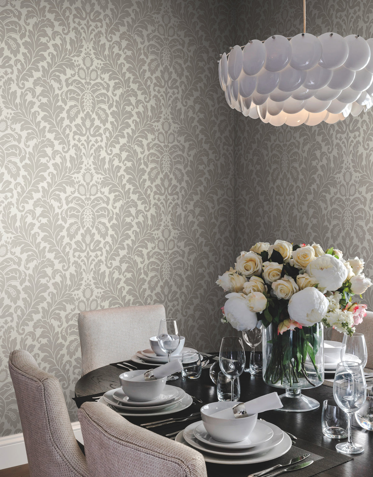 Dining room corner featuring light gray Candice Olson Modern Romance Wallpaper, a dark round table set for dinner, and a large vase of white peonies.