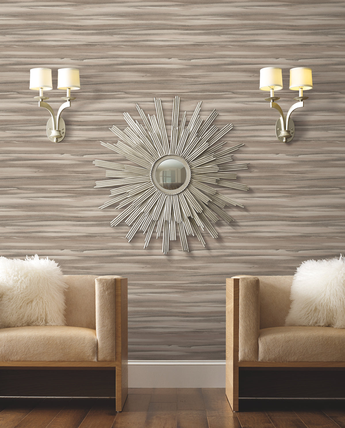 Two armchairs with fuzzy white pillows sit against a wall covered in Candice Olson Sanctuary Wallpaper, accented by a sunburst mirror and two wall sconces.