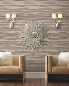 Two armchairs with fuzzy white pillows sit against a wall covered in Candice Olson Sanctuary Wallpaper, accented by a sunburst mirror and two wall sconces.