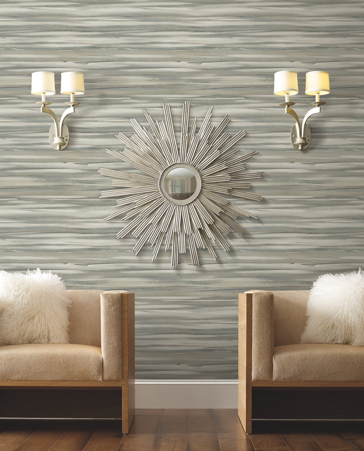 Candice Olson Sanctuary Wallpaper featuring a horizontal, brushstroke-style pattern in shades of gray, white, and blue, displayed behind two tan chairs and a sunburst mirror.