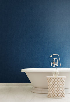 A deep blue Sweet Grass Wallpaper by York Wallcoverings installed behind a white freestanding bathtub and a small decorative side table.