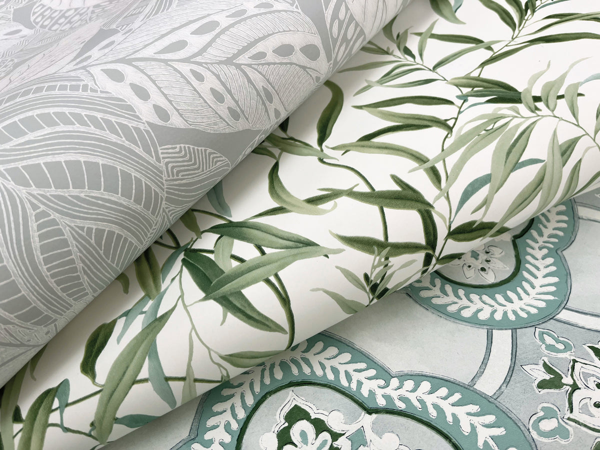 Three overlapping sheets of York Wallcoverings’ Willow Grove Wallpaper: one featuring gray leaf patterns, one showcasing green leafy vines, and one displaying blue and white ornate designs.