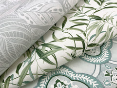 Three overlapping sheets of York Wallcoverings’ Willow Grove Wallpaper: one featuring gray leaf patterns, one showcasing green leafy vines, and one displaying blue and white ornate designs.