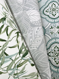 Three rolled wallpapers from York Wallcoverings: the Willow Grove Wallpaper featuring green leafy vines, a design with intricate gray and white leaves, and a pattern showcasing blue and white floral damask on a light blue background.