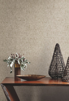 Ronald Redding Leather Lux Wallpaper in a neutral, small-scale geometric square pattern on a wall behind a wooden console table featuring a metal bowl, a vase with foliage, and two wire sculptures.