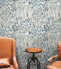 Ronald Redding Aspen Wallpaper featuring stylized cranes and spotted deer among blue and grey foliage on a light background, positioned between two leather chairs and a small round table.