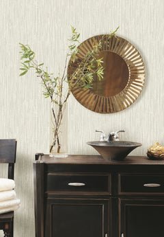 Off-white Ronald Redding Feather Fletch Wallpaper with a subtle vertical feather pattern behind a bathroom vanity featuring a dark wooden cabinet, a vessel sink, and a round sunburst mirror.