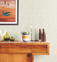 Light-colored Ronald Redding Feather Fletch Wallpaper featuring a vertical, feather-like pattern behind a wooden credenza holding a potted succulent, candlesticks, and decorative vases.