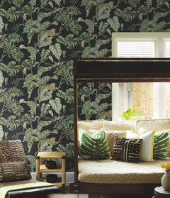 Ronald Redding Jungle Cat Wallpaper featuring a pattern of leopards, monkeys, and tropical leaves on a black background behind a daybed.