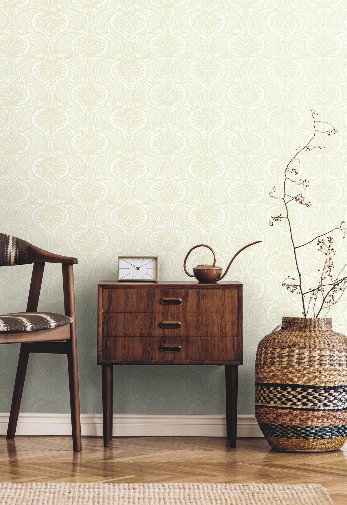 Ronald Redding Lotus Palm Wallpaper featuring a repeating white lotus and palm leaf pattern on a light green background, displayed behind a wooden side table, a chair, and a woven floor vase.