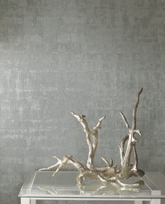 A metallic silver, textured Ronald Redding Liquid Metal Wallpaper background featuring a decorative silver driftwood sculpture resting on a glass table.