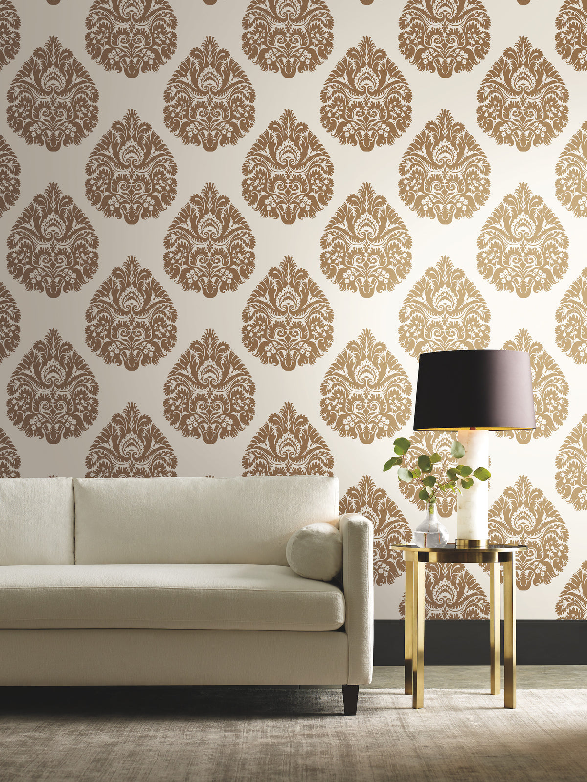 Off-white sofa and gold side table with a lamp against a wall covered in brown and white Ronald Redding Teardrop Damask Wallpaper.