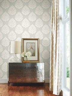 Ronald Redding Teardrop Damask Wallpaper in light gray with a repeating white teardrop damask pattern applied to a wall behind a dresser with a lamp and framed artwork.