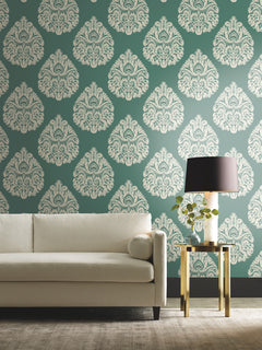 Ronald Redding Teardrop Damask Wallpaper featuring a repeating white teardrop-shaped pattern on a dark green background, displayed behind a white sofa and a side table with a lamp.