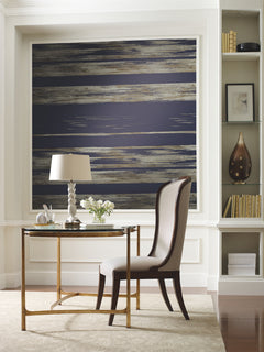 Ronald Redding Horizontal Dry Brush Wallpaper with horizontal dry brush stripes in dark blue, brown, and metallic tones installed on a wall behind a writing desk.