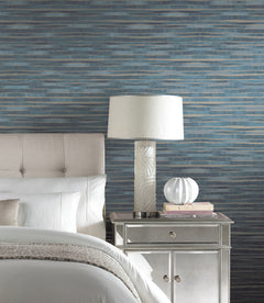 Ronald Redding Dreamscapes Wallpaper featuring horizontal, wavy bands of blue and gray behind a bedroom nightstand and lamp.