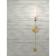 A modern gold-toned wall sconce with an exposed filament bulb mounted on Ronald Redding Dreamscapes Wallpaper featuring horizontal, textured grey and white brushstroke stripes.