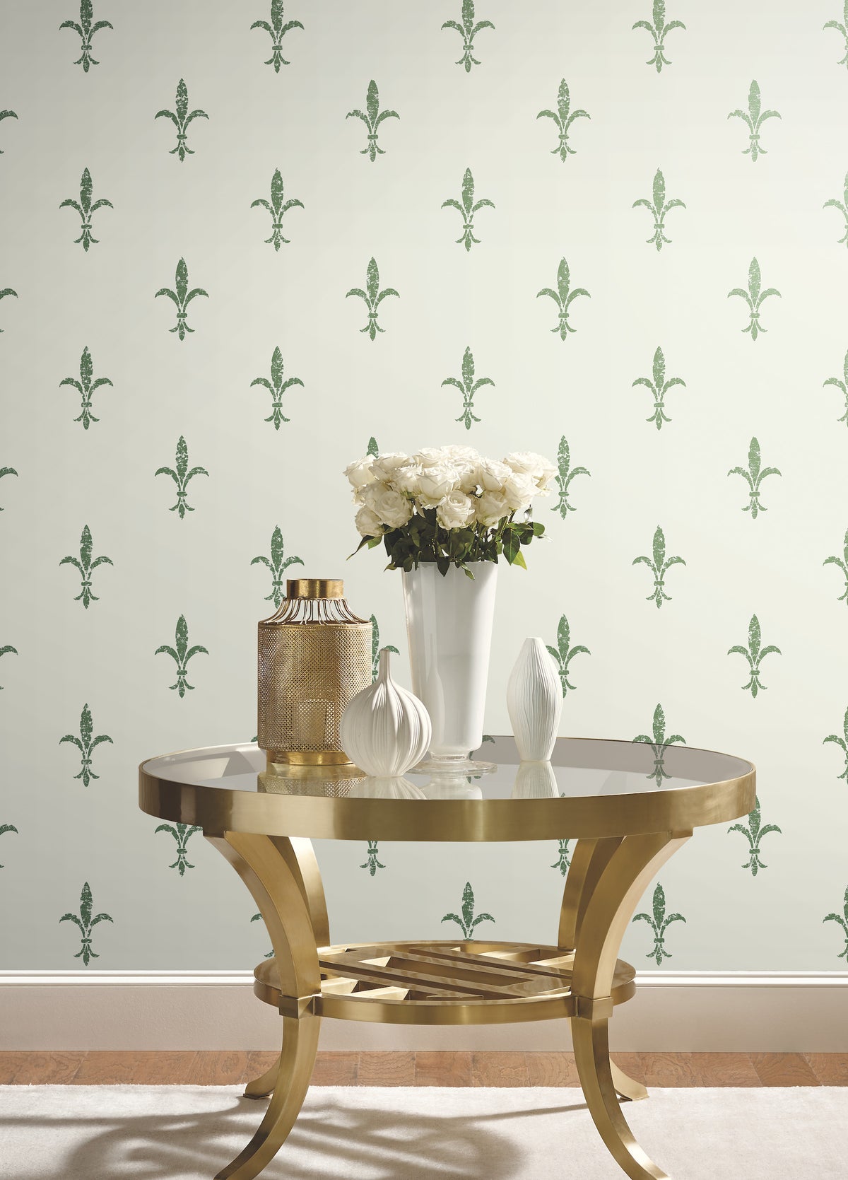 Ronald Redding Fleur De Lis Wallpaper in a repeating green pattern behind a round gold side table topped with a vase of white roses.