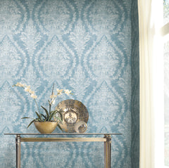 Ronald Redding Charleston Damask Wallpaper in blue with an ornate white floral pattern displayed behind a glass console table with a potted orchid and a decorative plate.