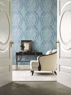 Blue Ronald Redding Charleston Damask Wallpaper with an intricate white pattern on a wall behind a console table and an armchair.