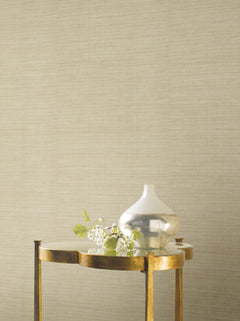 Ronald Redding Silk Elegance Wallpaper in beige, featuring a fine, horizontal fabric-like texture, shown behind a small metallic table holding a decorative vase and a small branch.