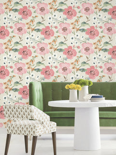 A white round table with yellow flowers in a vase, a white upholstered chair, and a green bench are arranged in front of a wall adorned with York Wallcoverings’ Evelyn Floral Wallpaper.