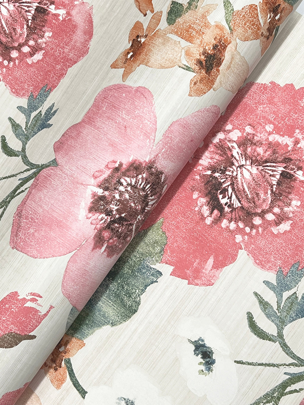 A close-up of Evelyn Floral Wallpaper by York Wallcoverings, featuring large pink and peach flowers with green leaves on a light, textured cream background and a visible folded crease running through the pattern.