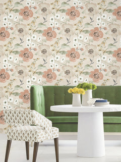 A green velvet bench and a white round table with small vases of yellow flowers sit in front of York Wallcoverings’ Evelyn Floral Wallpaper, with a patterned chair in the foreground.
