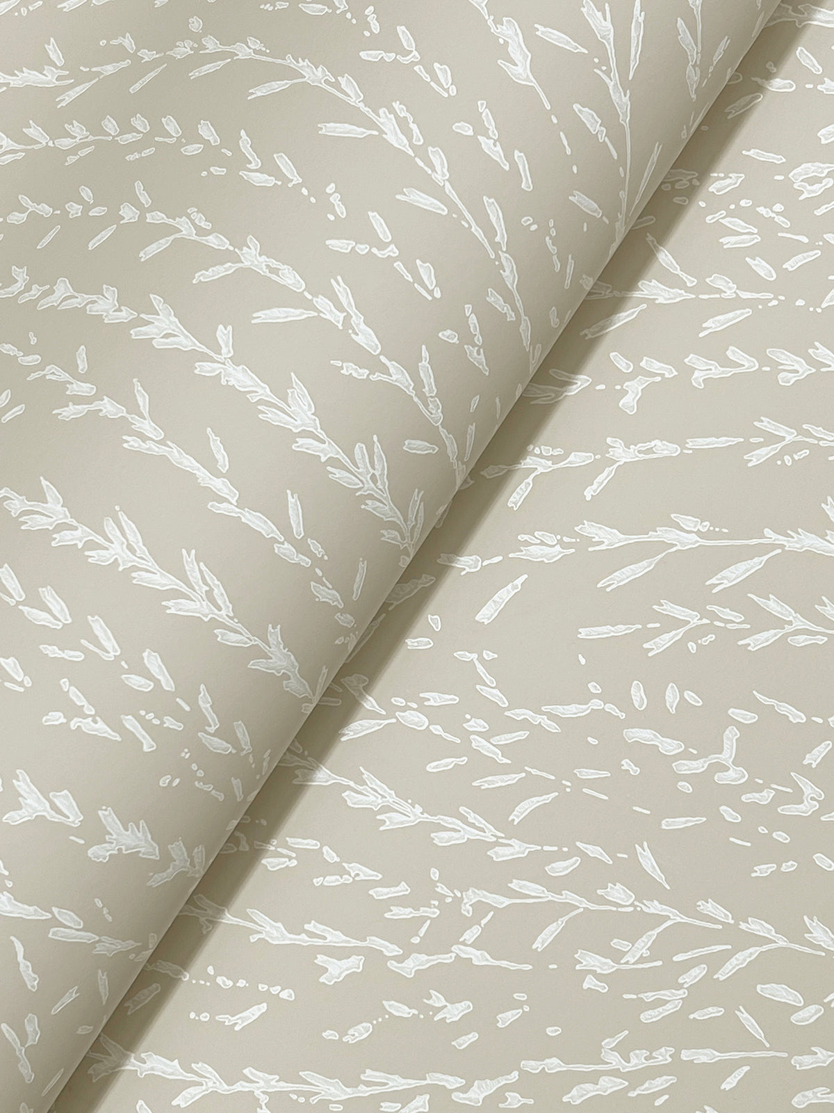 Willow Song Botanical Wallpaper by York Wallcoverings, shown rolled out at an angle, features a subtle white botanical pattern of delicate branches and leaves on a beige background.
