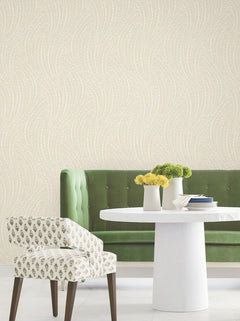 A green tufted sofa and patterned chair are arranged by a round white table topped with yellow and green floral arrangements, set against York Wallcoverings’ Willow Song Botanical Wallpaper in cream.