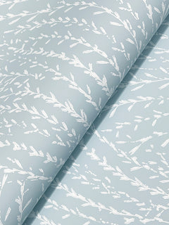 York Wallcoverings’ Willow Song Botanical Wallpaper features a light blue background adorned with a white, abstract leafy branch motif. The wallpaper displays a gently folded texture, highlighting its elegant repeating botanical design.