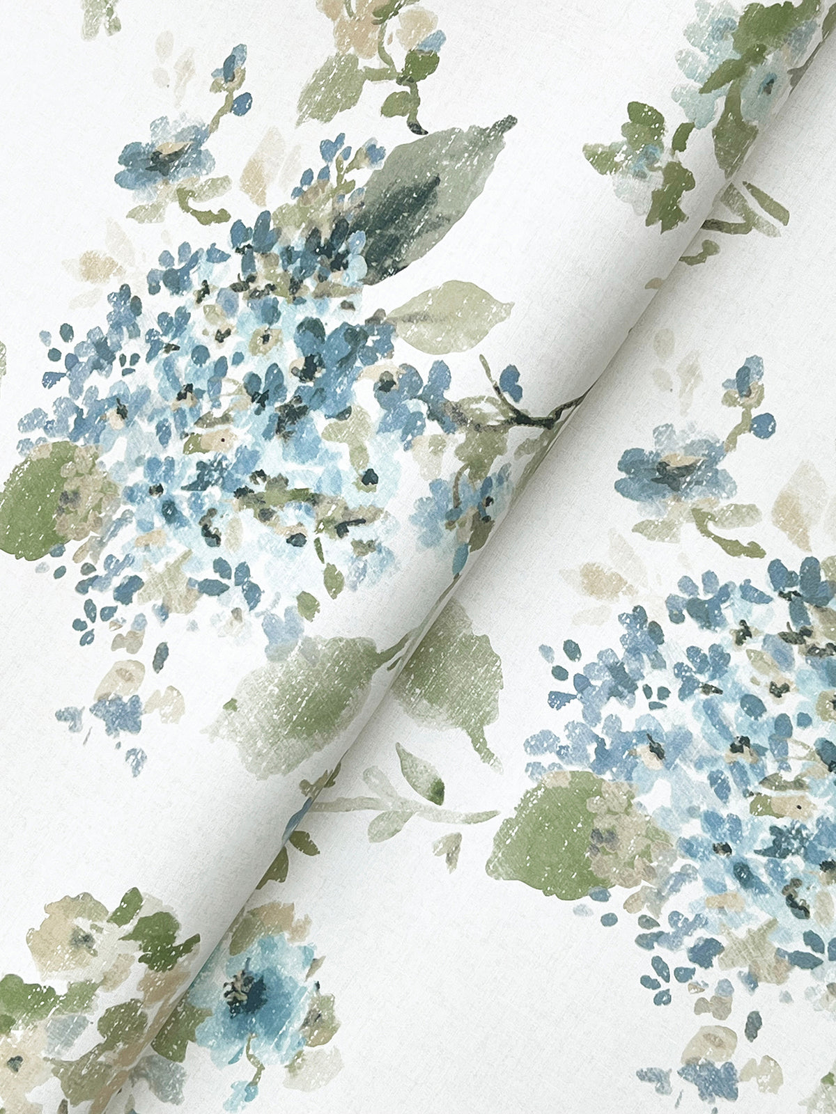 Veiled Garden Floral Wallpaper by York Wallcoverings features a watercolor-style floral print with clusters of blue and green flowers and leaves on a white background. The wallpaper is shown slightly folded diagonally across the image.