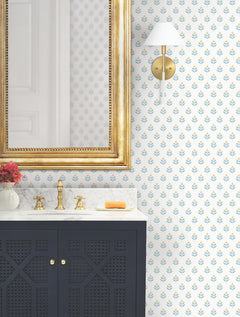 Bathroom featuring a gold-framed mirror, black vanity with marble countertop, brass faucet, soap, sconce light, and a vase with pink flowers on the counter. The walls are adorned with Serene Villa Floral Stamp Wallpaper by York Wallcoverings.